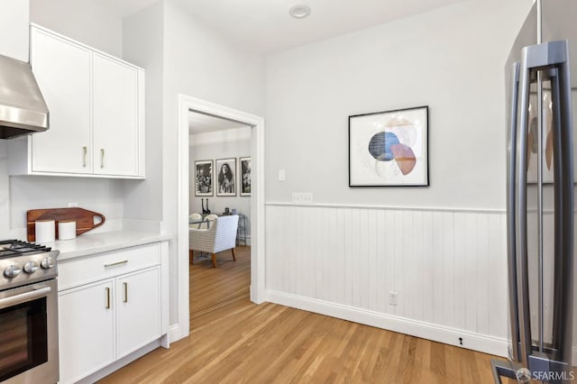 kitchen featuring light countertops, white cabinets, stainless steel gas stove, and wall chimney exhaust hood