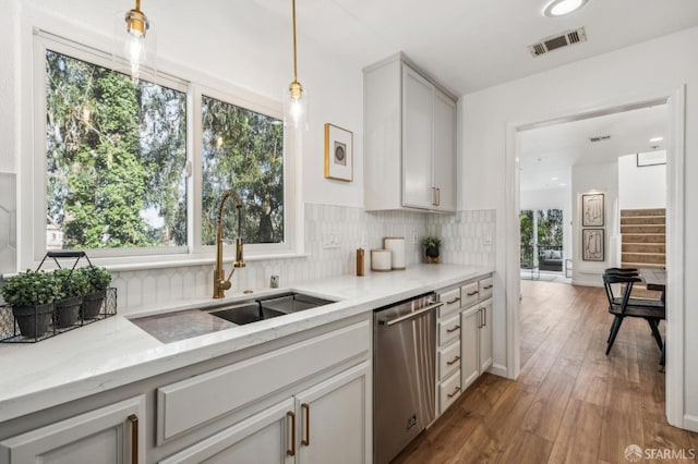 kitchen featuring visible vents, decorative backsplash, hardwood / wood-style floors, stainless steel dishwasher, and a sink