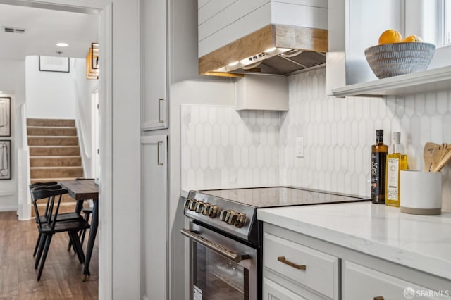 kitchen with visible vents, decorative backsplash, light stone counters, stainless steel electric stove, and premium range hood