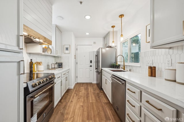 kitchen featuring light wood-style flooring, stainless steel appliances, a sink, decorative backsplash, and pendant lighting