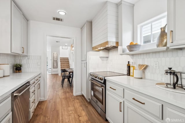 kitchen with custom exhaust hood, visible vents, appliances with stainless steel finishes, light wood-style floors, and light stone countertops