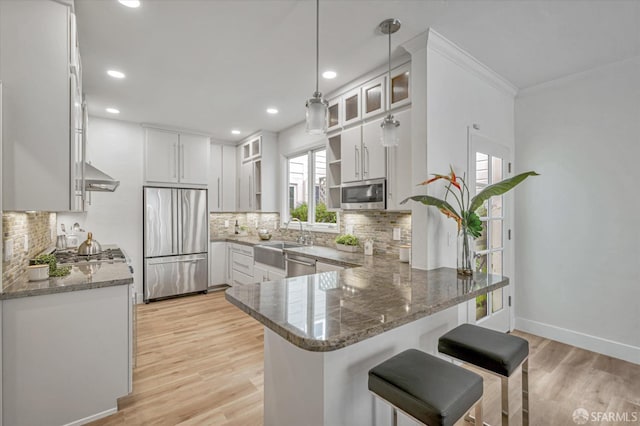 kitchen featuring white cabinetry, hanging light fixtures, stainless steel appliances, kitchen peninsula, and dark stone counters