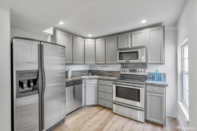 kitchen featuring gray cabinetry, stainless steel appliances, dark stone countertops, and light wood-type flooring