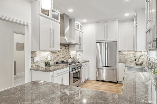 kitchen featuring white cabinetry, sink, dark stone counters, stainless steel appliances, and wall chimney range hood