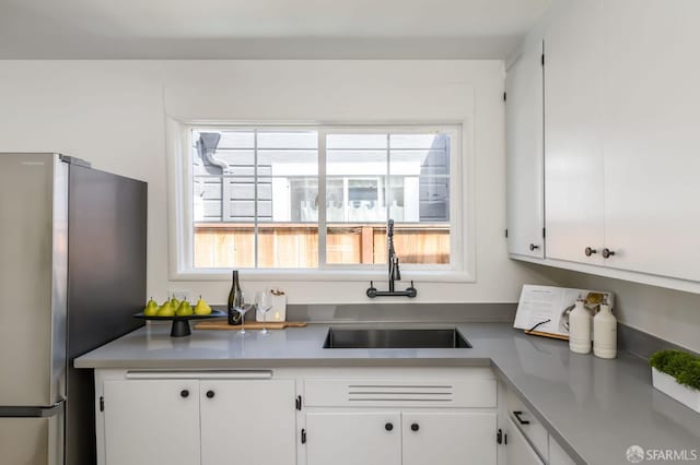 kitchen featuring a sink, light countertops, freestanding refrigerator, and white cabinetry