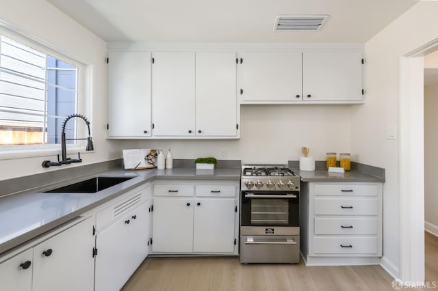 kitchen with a sink, gas stove, white cabinets, and visible vents