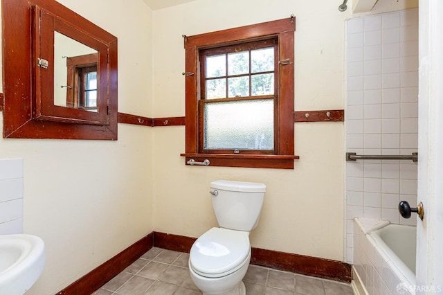 bathroom featuring tile patterned floors, baseboards, toilet, and a relaxing tiled tub