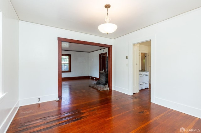 spare room featuring wood-type flooring, baseboards, and a wood stove