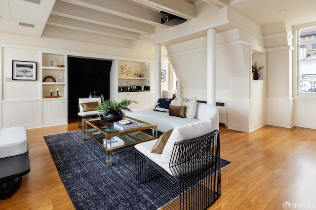living room featuring built in features, visible vents, light wood-style flooring, and wainscoting