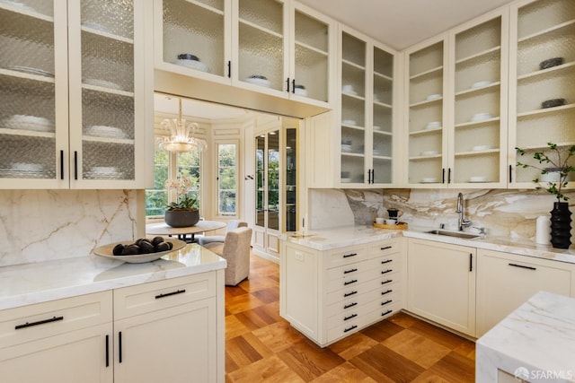 kitchen with decorative backsplash, glass insert cabinets, light stone countertops, and a sink