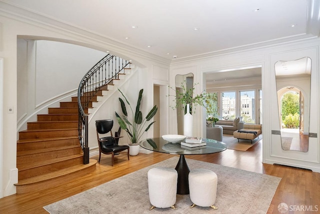 foyer with stairs, a decorative wall, wood finished floors, and ornamental molding