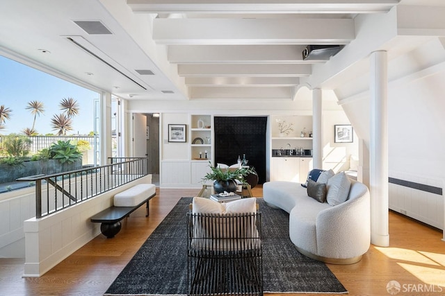 living area with built in shelves, wood finished floors, visible vents, beam ceiling, and radiator heating unit
