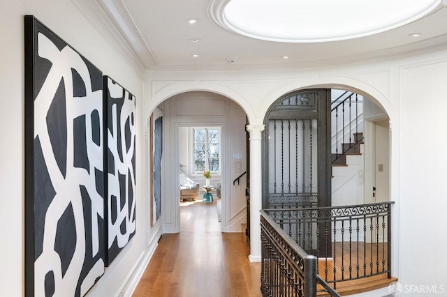 hall with stairway, wood finished floors, recessed lighting, arched walkways, and ornamental molding