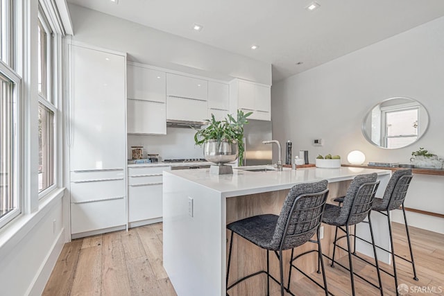 kitchen featuring modern cabinets, an island with sink, light wood-style flooring, white cabinetry, and a breakfast bar area