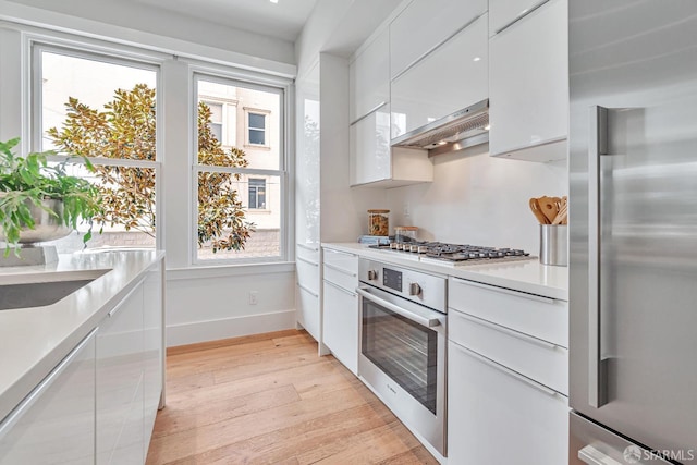 kitchen featuring modern cabinets, white cabinetry, stainless steel appliances, light wood-style floors, and light countertops