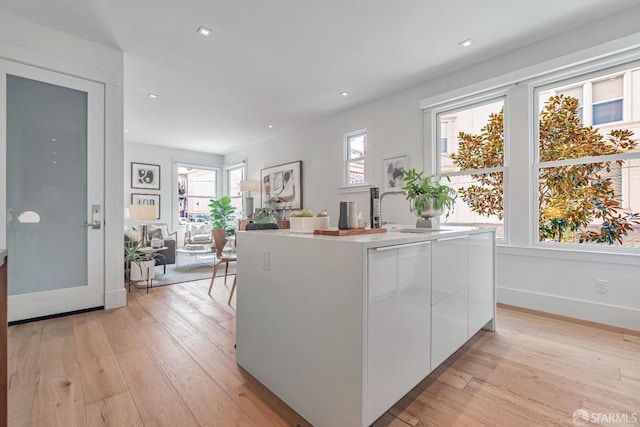 kitchen featuring light wood-style floors, modern cabinets, a center island with sink, and white cabinetry