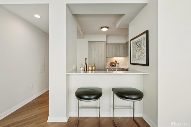 bar featuring baseboards, decorative backsplash, wood finished floors, and recessed lighting