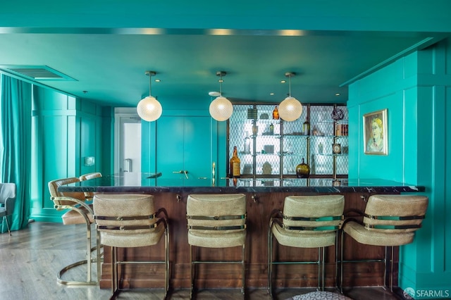 bar featuring bar, a decorative wall, decorative light fixtures, wood finished floors, and visible vents