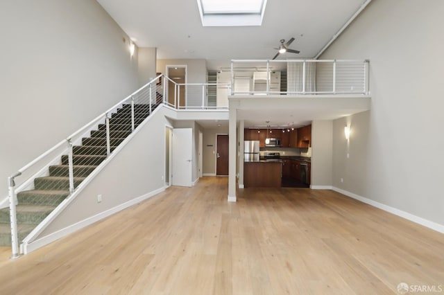 unfurnished living room with a towering ceiling, a skylight, light hardwood / wood-style floors, and ceiling fan