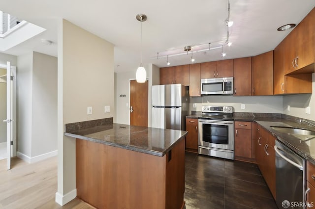 kitchen with sink, appliances with stainless steel finishes, dark stone countertops, hanging light fixtures, and kitchen peninsula