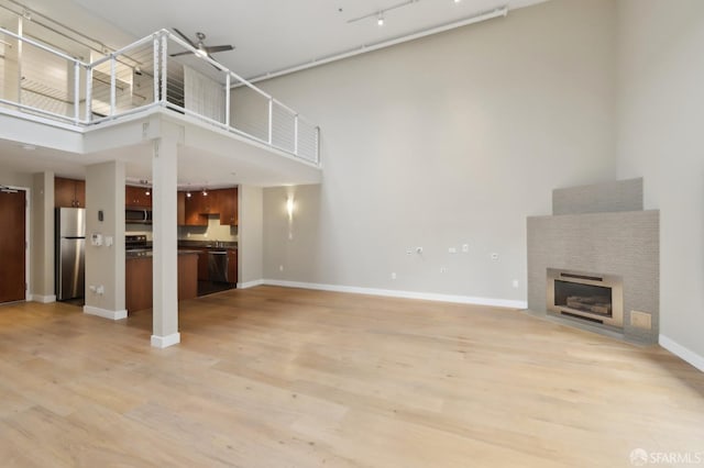 unfurnished living room featuring track lighting, light hardwood / wood-style floors, and a high ceiling