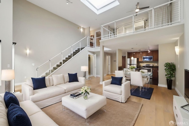 living room with a high ceiling, rail lighting, light wood-type flooring, and a skylight