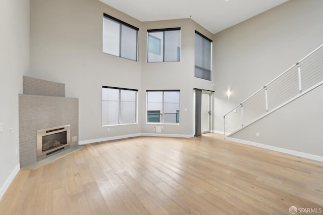 unfurnished living room featuring a towering ceiling, a fireplace, and light hardwood / wood-style floors