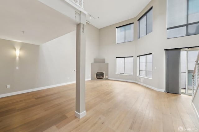 unfurnished living room featuring a towering ceiling, track lighting, and light hardwood / wood-style floors