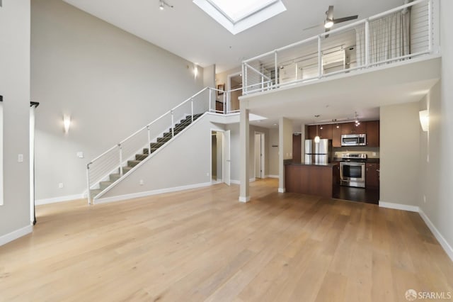 unfurnished living room with a towering ceiling, track lighting, light wood-type flooring, and a skylight