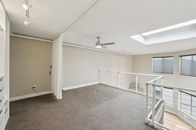 spare room featuring dark colored carpet, rail lighting, ceiling fan, and a skylight