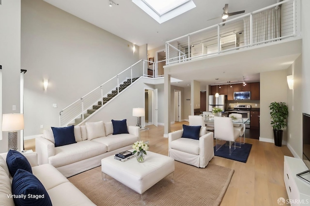 living room featuring a towering ceiling, rail lighting, a skylight, and light wood-type flooring