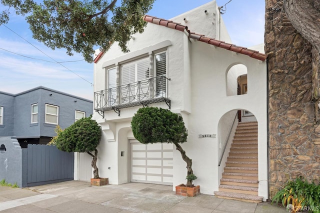 mediterranean / spanish house featuring driveway, a balcony, a tiled roof, an attached garage, and stucco siding