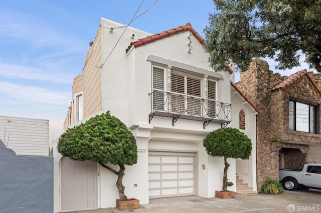 view of front of house featuring a balcony, a garage, a tile roof, concrete driveway, and stucco siding