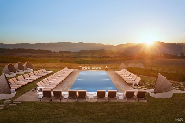 pool at dusk featuring a mountain view, a patio area, and a lawn