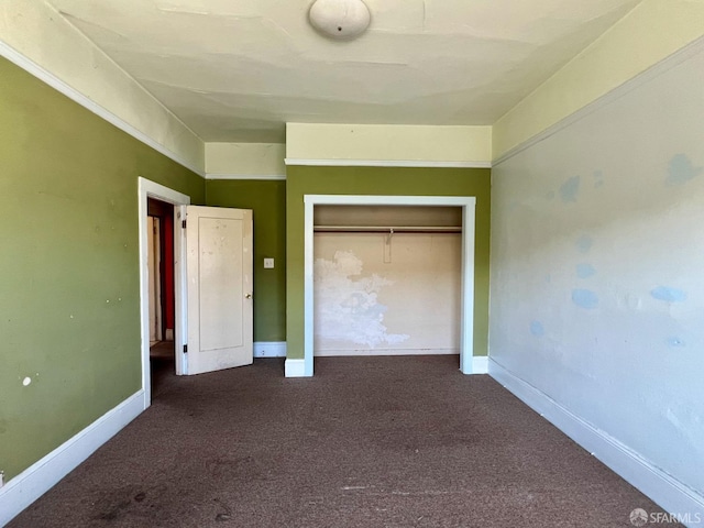unfurnished bedroom with dark colored carpet, a closet, and baseboards