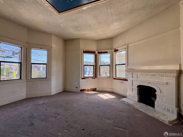 unfurnished living room featuring carpet, a fireplace with raised hearth, a textured ceiling, and baseboards