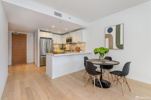 kitchen with kitchen peninsula, appliances with stainless steel finishes, tasteful backsplash, light hardwood / wood-style flooring, and white cabinets