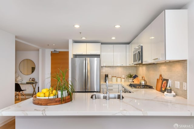 kitchen featuring white cabinets, sink, appliances with stainless steel finishes, tasteful backsplash, and kitchen peninsula