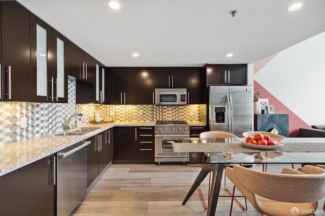 kitchen featuring light stone countertops, appliances with stainless steel finishes, light wood-type flooring, dark brown cabinetry, and sink