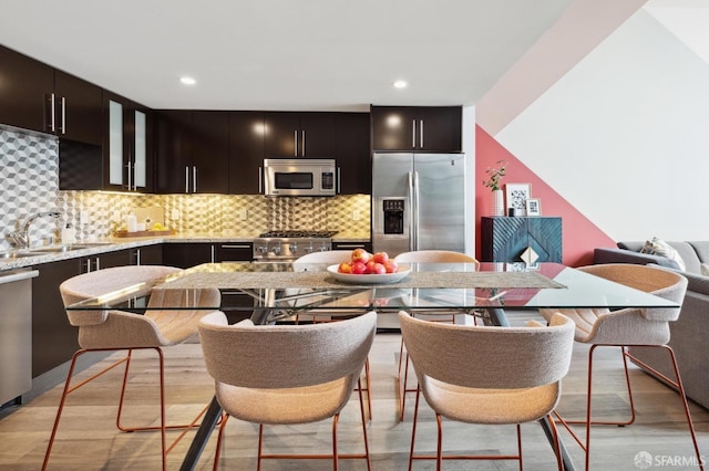 kitchen with sink, light wood-type flooring, appliances with stainless steel finishes, tasteful backsplash, and dark brown cabinets