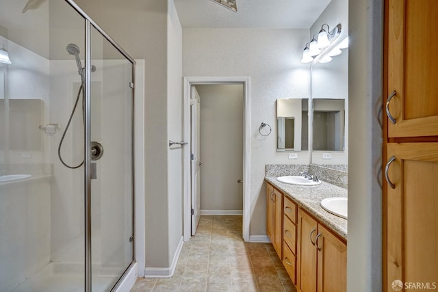 bathroom with a stall shower, double vanity, baseboards, and tile patterned floors