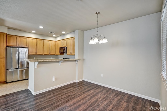 kitchen featuring freestanding refrigerator, black microwave, a kitchen breakfast bar, wood finished floors, and baseboards