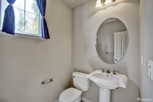 half bathroom with toilet, a sink, and baseboards