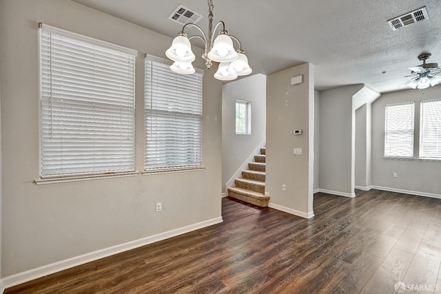 empty room with a chandelier, wood finished floors, healthy amount of natural light, ceiling fan, and a textured ceiling