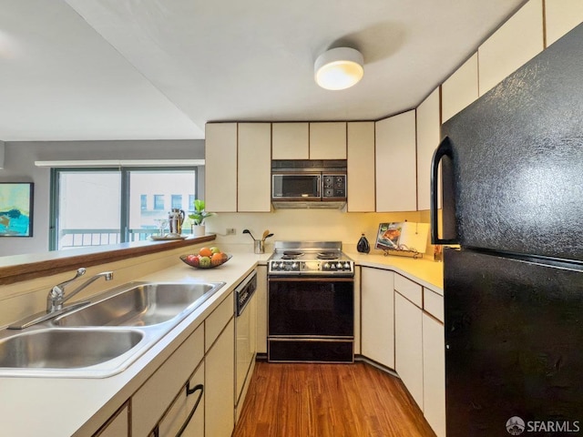 kitchen with light countertops, electric range oven, freestanding refrigerator, a sink, and wood finished floors