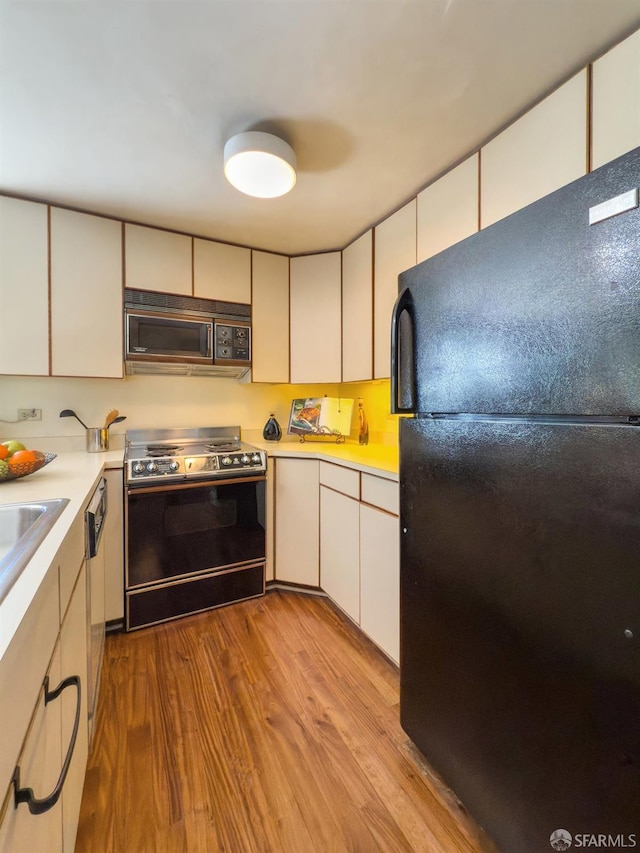 kitchen with black appliances, white cabinetry, light countertops, and wood finished floors