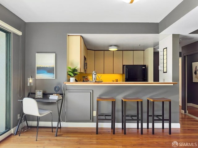 kitchen featuring wood finished floors, baseboards, freestanding refrigerator, stainless steel microwave, and a kitchen bar