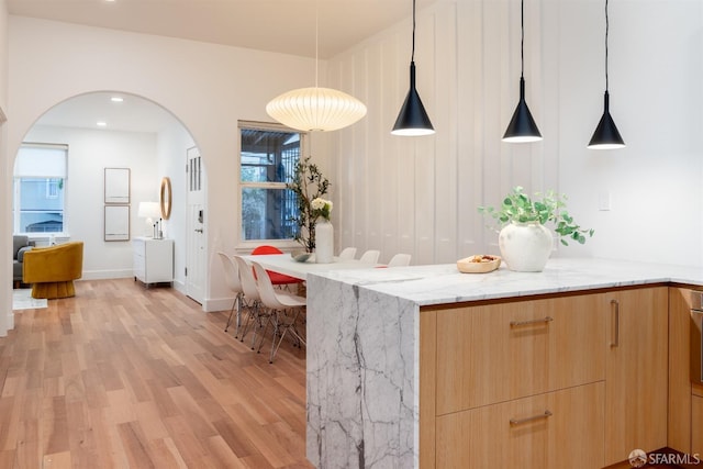 interior space with decorative light fixtures, light hardwood / wood-style floors, and light stone countertops