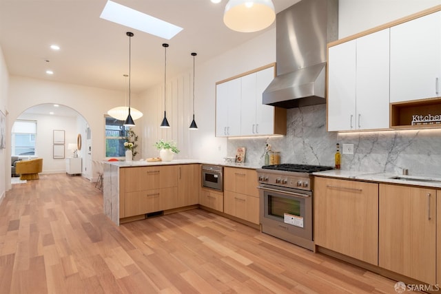 kitchen with decorative light fixtures, backsplash, high end range, white cabinetry, and wall chimney exhaust hood