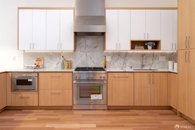 kitchen with wall chimney range hood, stainless steel appliances, decorative backsplash, sink, and light wood-type flooring